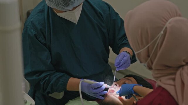 Dental team using scaler and suction tools to treat patient teeth in clinic