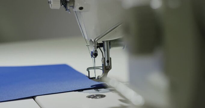 Industrial sewing machine needle stitching blue fabric in manufacturing workshop