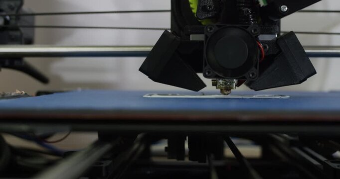 A 3d printer nozzle moves and extrudes plastic filament to build a layered object on a platform