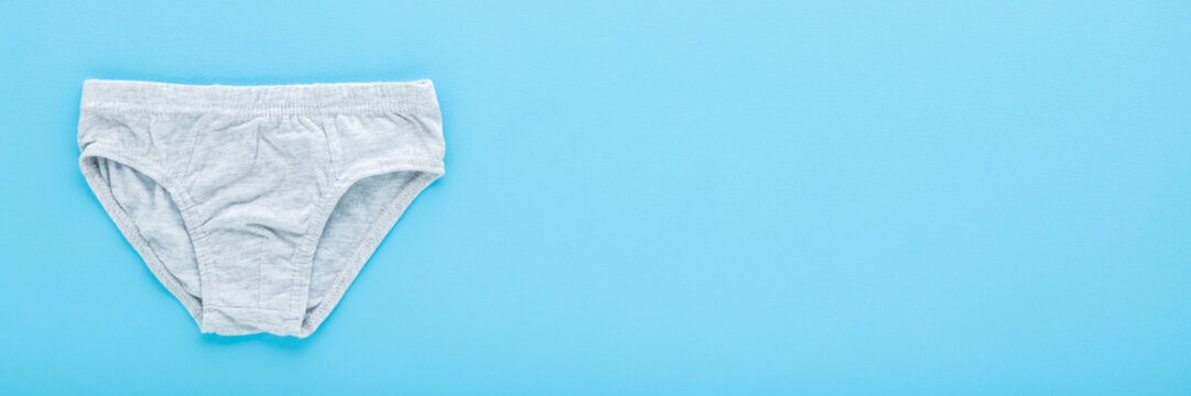 New light gray panties for little child boy on light blue table background. Pastel color. Closeup. Wide banner. Empty place for text.  Flat lay. Top down view.