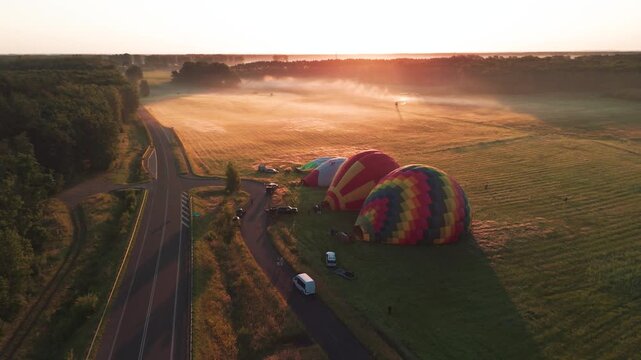 Cinematic aerial shot of colorful hot air balloons inflating in a misty field during a beautiful sunrise. Perfect for travel, adventure, and wellness content.