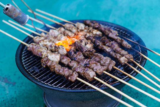 Delicious Meat Skewers Grilling on a Small Charcoal Barbecue with Flames