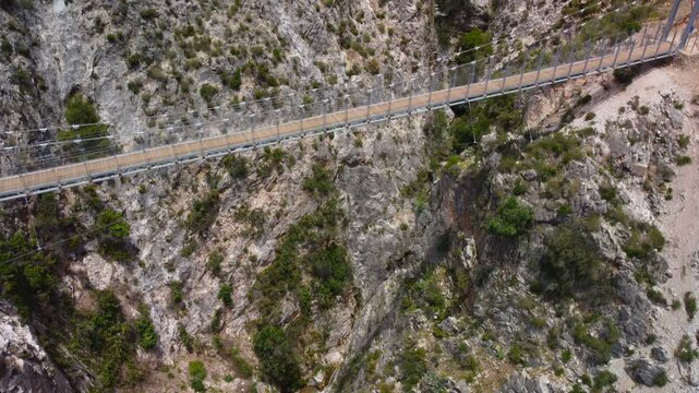 Aerial view of suspension bridge of 'El Saltillo Canillas de Aceituno' in the beautiful mountain landscape of Canillas de Aceituno on a sunny day, Malaga, Spain