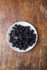 ripe fresh blackberries in white plate on brown old rustic wooden table, top view, copy space © Olena Seiryk