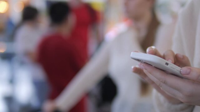 Person holds smartphone, focused on screen, ignoring surroundings. Background shows blurred people in public space. Scene captures modern connectivity and distraction. Ideal for tech, lifestyle