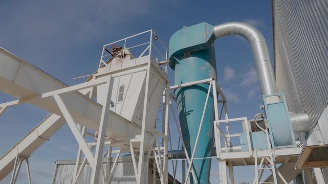 Outdoor wood processing system with cyclone separator, ducts, conveyors, and metal structures under blue sky