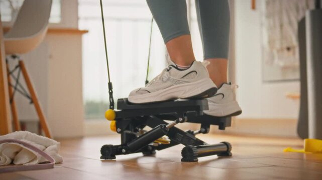 In a home gym, a girl wearing leggings and white sneakers exercises on a stepper, demonstrating effective cardio training at home. She moves rhythmically, using the stepper for a convenient workout