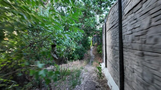 Walking down the scenic dirt path past dry summer grass and lush green trees toward a beautiful country house with a prominent red roof. Amazing cinematic stock shot in 4K 24fps with Motion Blur.
