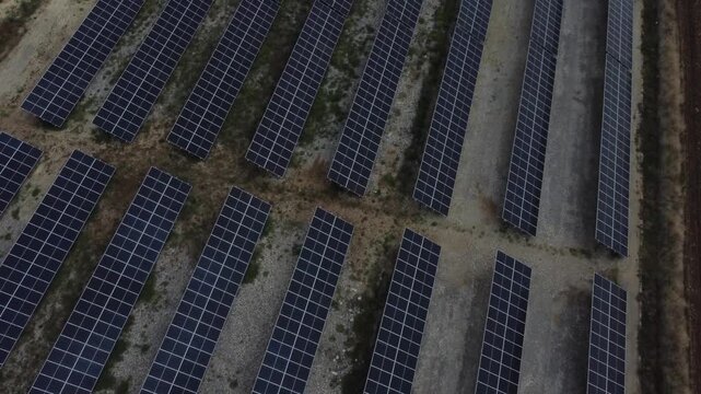 Aerial tracking shot of solar panel arrays stretching across rural farmland with aligned photovoltaic rows and service huts