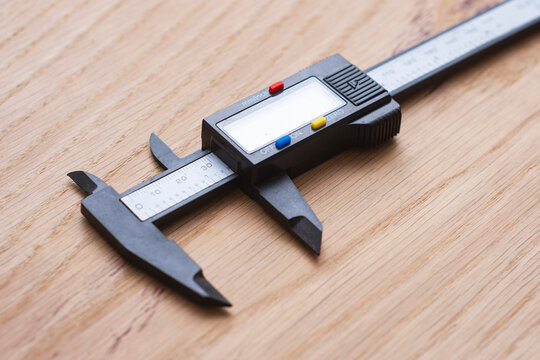 Digital caliper on a wooden surface for technical or industrial design. Precision measuring tool for engineering, machining, quality control, manufacturing, woodworking and workshop applications.