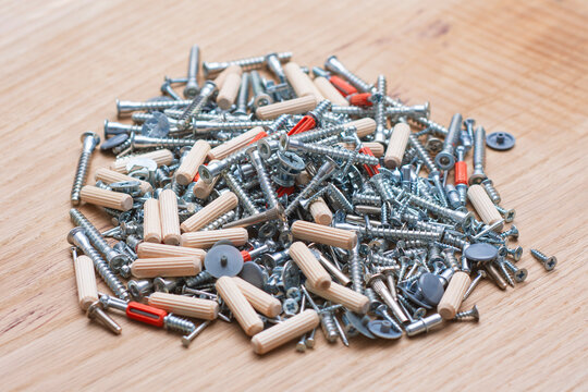 Pile of mixed furniture assembly hardware with screws, dowels and fasteners on wooden surface. Hardware store and furniture manufacturing guides.
