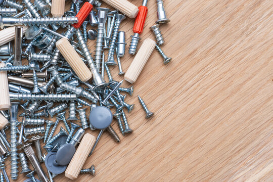 Furniture assembly hardware kit with metal screws, wooden dowels and fasteners on wood background copy space. Carpentry, flat pack diy joinery or home remodeling construction concept.