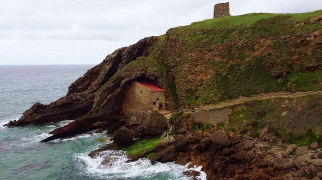 Aerial drone view of Santa Justa Hermitage, a unique chapel built inside a coastal cliff cave in Ubiarco, near Santillana del Mar, Cantabria, Northern Spain. High quality 4k footage