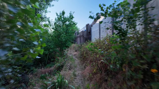 Walking down the scenic dirt path past dry summer grass and lush green trees toward a beautiful country house with a prominent red roof. Amazing cinematic stock shot in 4K 24fps with Motion Blur.