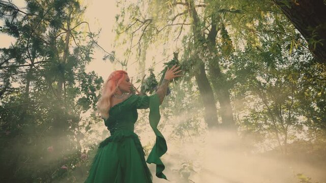 fantasy woman healer hand touches bunches of dry grass, dries medicinal herbs bouquets flowers plants for essential oil. Fairy elf girl green dress. forest summer nature trees magic sun rays light fog