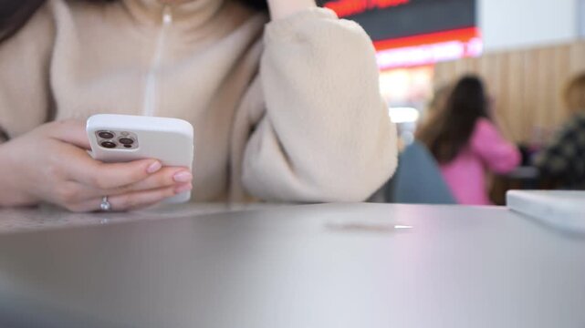 Woman sits at table, focused on phone. Soft light highlights her calm expression. Casual setting suggests quiet moment. Could fit digital marketing, lifestyle, or social media content