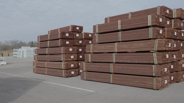 Large stacks of bundled wooden boards stored outdoors in an industrial lumber yard under cloudy sky