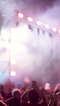 vertical shot. A crowd of people is dancing and cheering at a live music concert. Bright, multicolored stage lights illuminate the audience. An energetic atmosphere and a thrilling live performance.