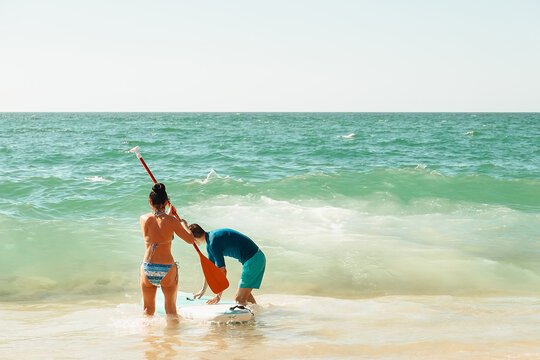 beach Ursa, Portugal.  friends are paddleboarding in ocean on a sunny day. They are in shallow water near the beach, enjoying time together as they interact and prepare for their ride.