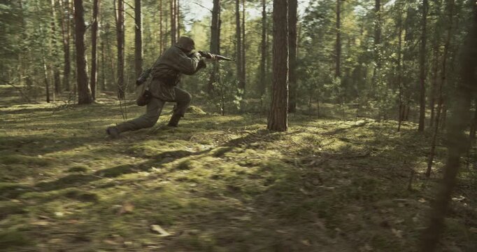 Reenactor Dressed As German Infantry Soldier, Assault Run And Aiming From Rifle Carabine Mauser 98k In Forest. War Combat In Forest. Reenactment Tactic Game. Wermacht Military Uniform