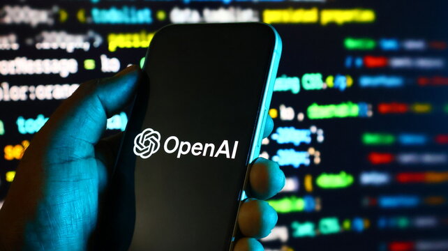 Smartphone displaying openai logo held in hand with computer code background in darkness.