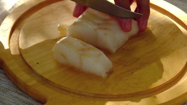 A chef cuts cod or other white fish fillets into strips on a board against a white background outdoors. Step-by-step video recipes. Ingredients for cooking