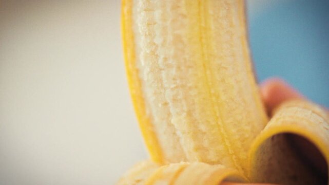 A man's hands carefully peel a fresh banana, revealing the detailed texture of the flesh in close-up. A natural snack being prepared in a home kitchen on a bright sunny day. Healthy eating concept