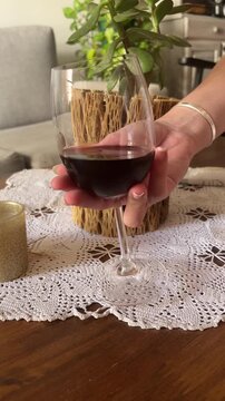 Young woman' hand wirling a glass of red wine in a cosy living room experiencing the aroma and flavour of the beverage
