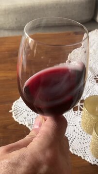 Man's hand  swirling a glass of red wine in a sunny room, enjoying the aroma and flavour of the drink.