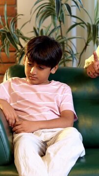 Indian mother scolding son while sitting in modern home on sofa, teaching good habits, inculcating discipline, bonding in quality time, guiding child with love, parent child relationship indoors