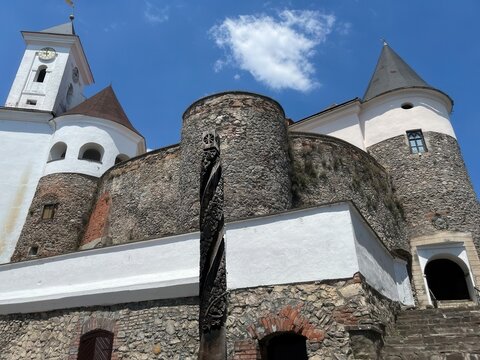 Low angle view of medieval castle clock tower and round stone bastions with carved wooden totem pole against blue sky with clouds. Concept of European heritage architecture and historic landmark explo