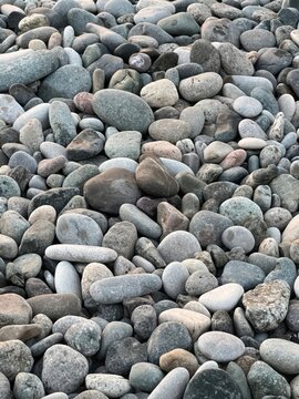 Smooth gray pebbles covering rocky beach surface with natural stone texture and coastal background