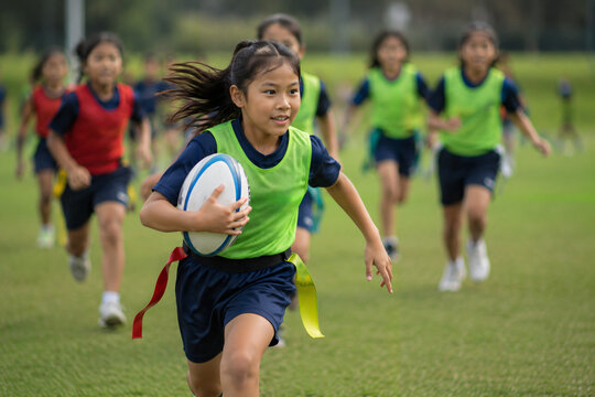 Young girl running with a rugby ball during a flag football match on the field