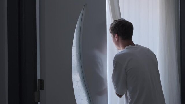 Modern world uncertainty and quiet dystopian anxiety concept with man looking through curtain in daylight apartment, psychological tension and safe home vs outside world fear