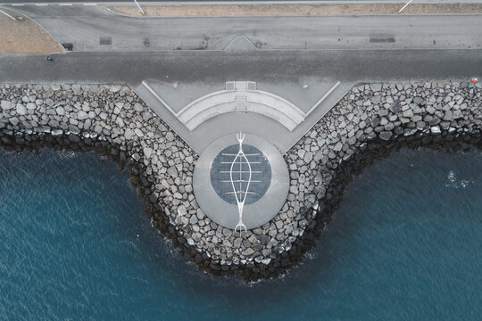 Aerial view of the Sun Voyager sculpture on a stone promenade, featuring a metal Viking ship structure near dark volcanic rocks and the Atlantic Ocean in Reykjavik, Reykjavikurborg, Iceland.