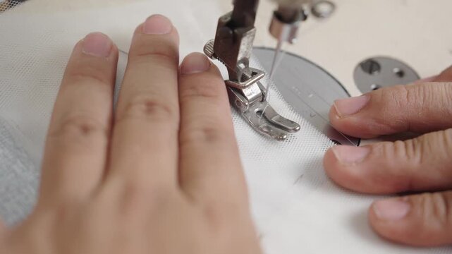 Macro close-up of sewing machine presser foot stitching bridal fabric for custom wedding dress
