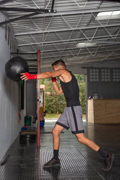 Young Hispanic boxer throwing medicine ball against wall in gym