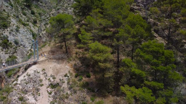 Aerial view of suspension bridge of 'El Saltillo Canillas de Aceituno' in the beautiful mountain landscape of Canillas de Aceituno on a sunny day, Malaga, Spain