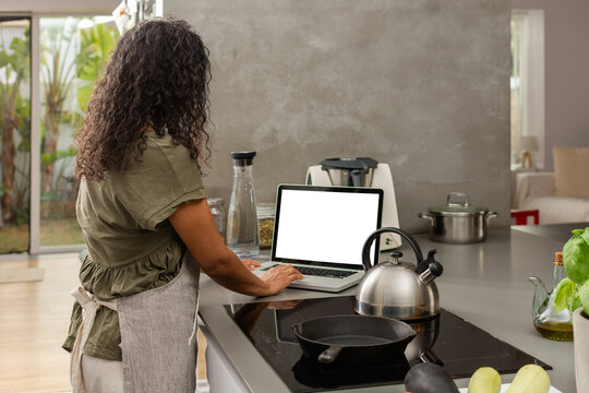 Rear view of woman using laptop in modern kitchen workspace