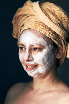 Woman with facial mask and towel on head enjoying skincare routine
