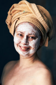 Woman with facial mask and towel on head enjoying skincare routine