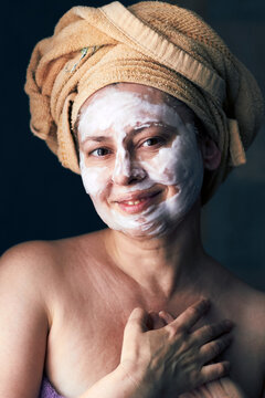 Woman with facial mask and towel on head enjoying skincare routine