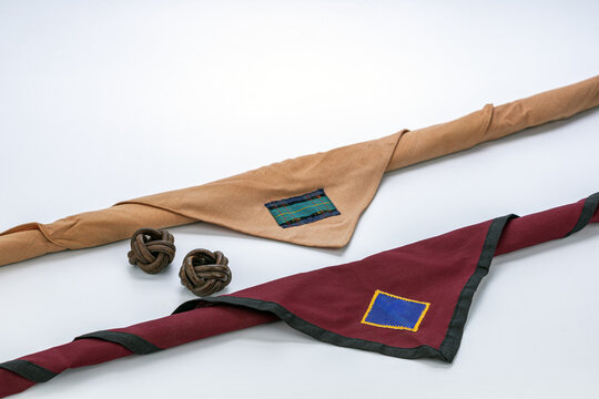 Traditional Thai scout uniform accessories featuring tan and maroon neckerchiefs with colorful badge patches arranged alongside two handcrafted leather Turk's head woggles on a clean white background