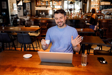 Fototapeta premium Man works on laptop while holding cup in busy cafe during afternoon