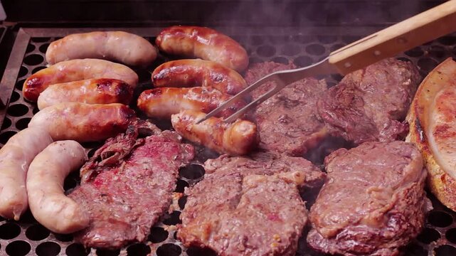 Juicy chicken sausage being pierced by a long fork on the grill alongside beef steaks amidst the smoke.