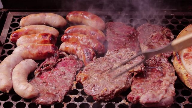 A juicy beef steak being pierced by a long fork on the grill alongside sausages amidst the smoke