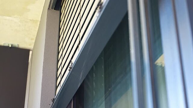 Exterior window blinds automatically closing over a large apartment window. Smart home automation and energy efficient sun protection concept.
