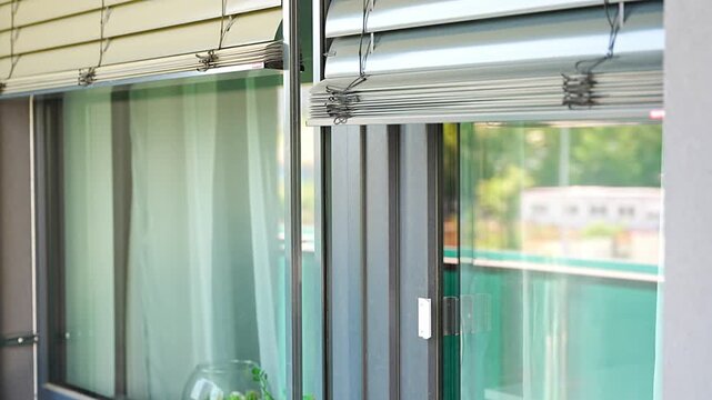 Exterior window blinds automatically closing over a large apartment window. Smart home automation and energy efficient sun protection concept.