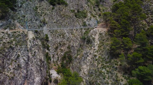Aerial view of suspension bridge of 'El Saltillo Canillas de Aceituno' in the beautiful mountain landscape of Canillas de Aceituno on a sunny day, Malaga, Spain