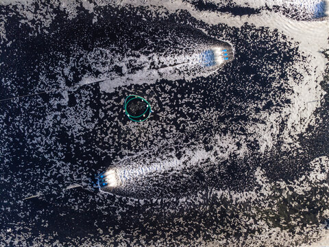 Aerial view of Pantai Pasir featuring two boats creating wakes in the water near a circular fish farm structure in Kecamatan Ayah, Jawa Tengah, Indonesia.